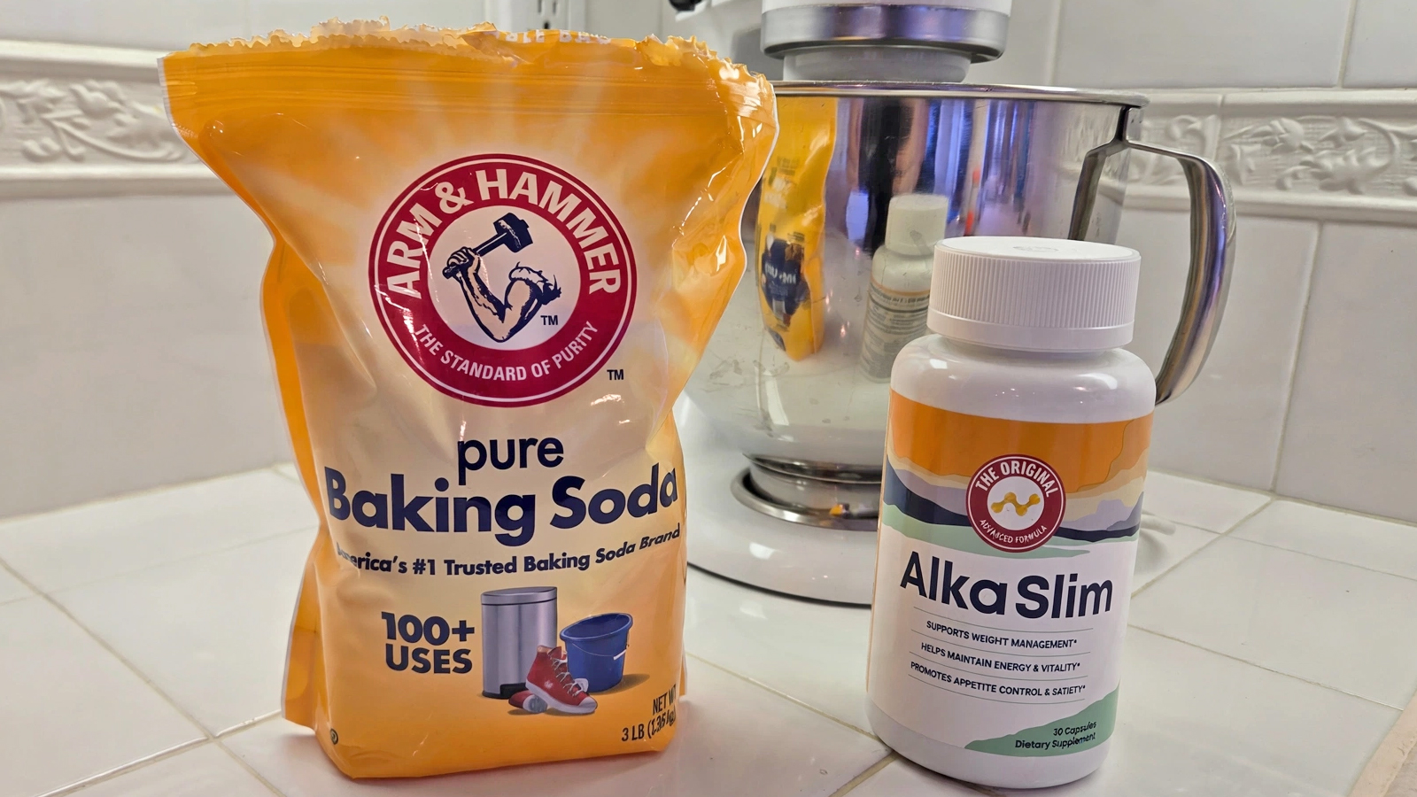 An image shows a bag of Arm & Hammer pure baking soda next to a bottle of AlkaSlim weight loss supplements, all in a kitchen counter setting in front of a KitchenAid mixer.